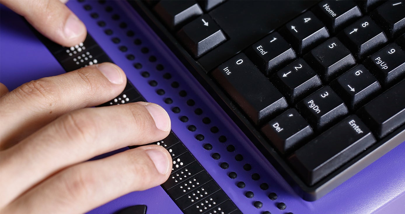 A person types on a purple Braille keyboard