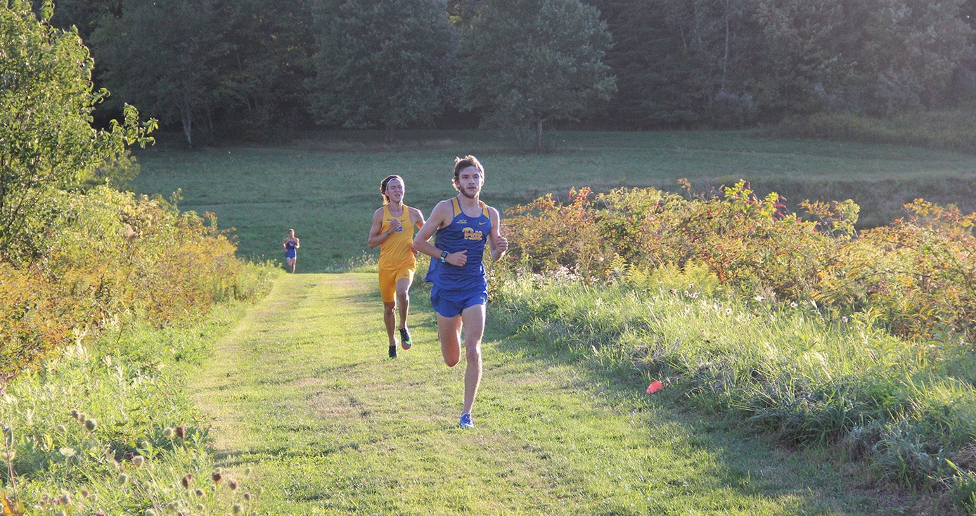 Two runners in Pitt attire in a field