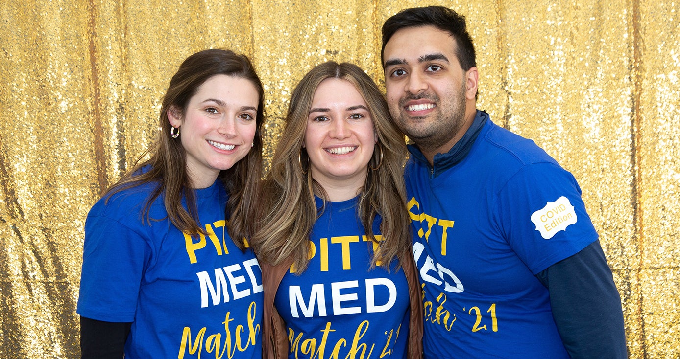 Three students in blue Pitt Med Match t-shirts.  Behind them is a gold background.