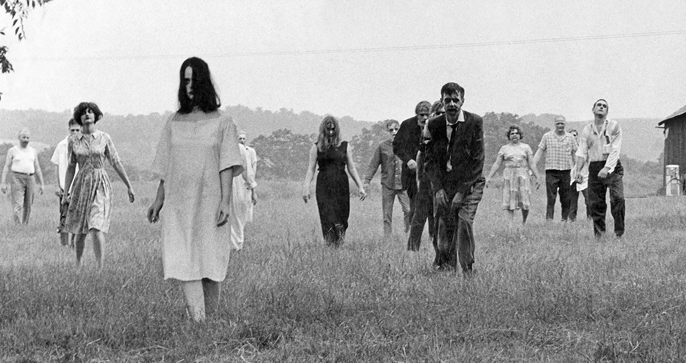 Black and white film still from "Night of the Living Dead" showing several zombies crossing a field