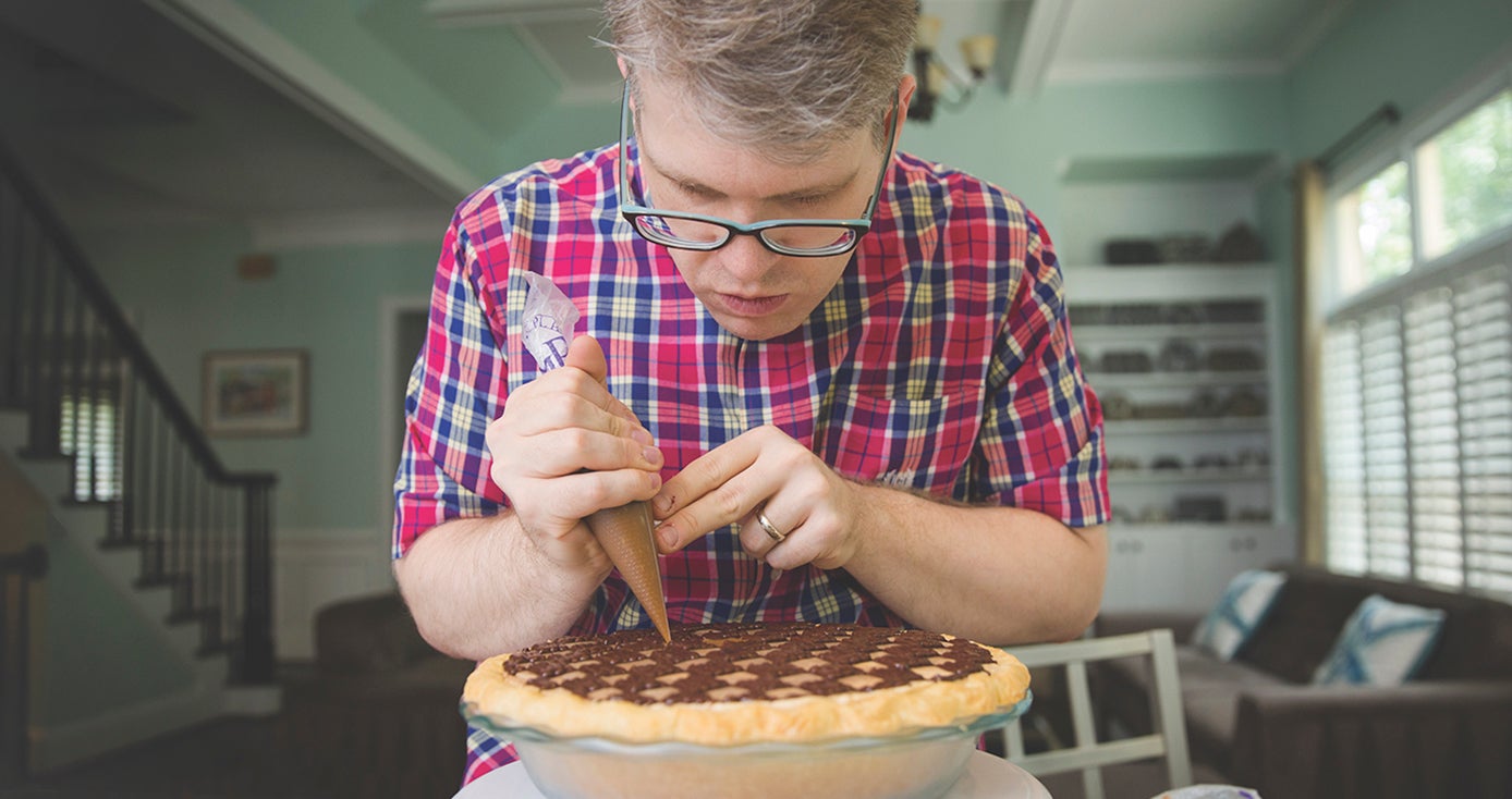 Pitt alumnus Chris Taylor in plaid shirt, using a pastry bag to finish work on a peanut butter checkerboard pie