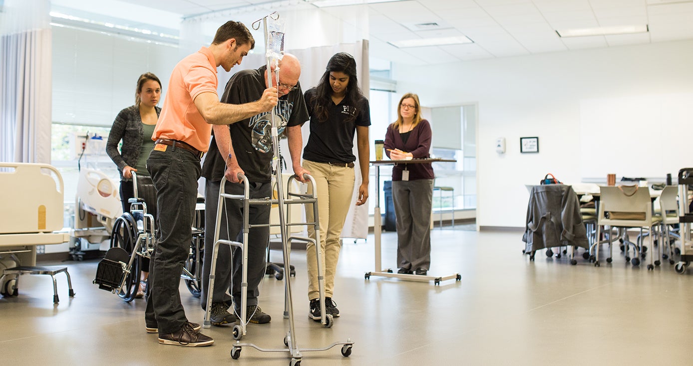 Therapists assist a person in a walker. 