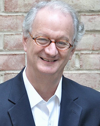 A man with glasses and a gray-blue jacket over a white shirt