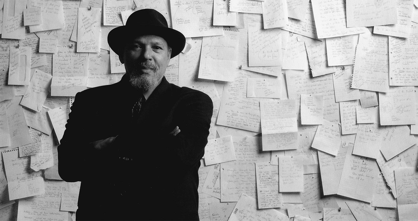 A man in a black coat and hat in front of a wall covered in paper