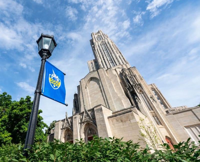 A black street light with a University of Pittsburgh banner sits in the foreground in front of the Cathedral of Learning.