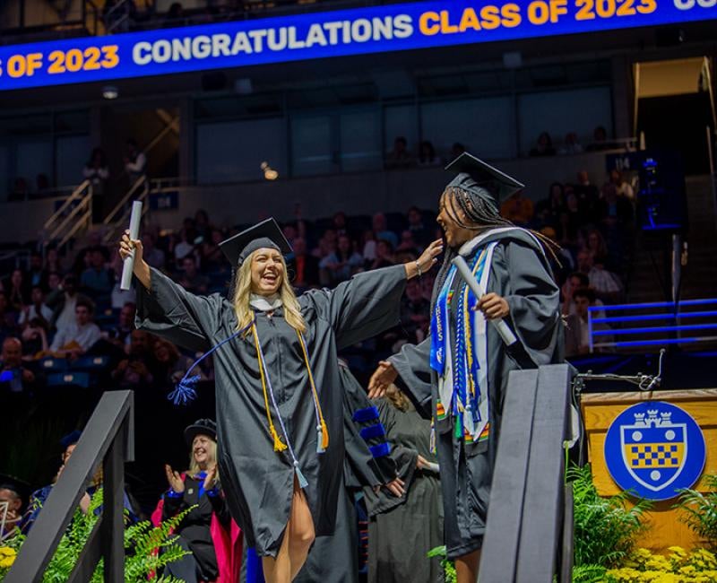 Two graduates celebrate after they cross the stage at Pitt's commencement