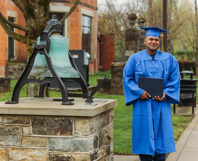 A graduate stands next to a large bell