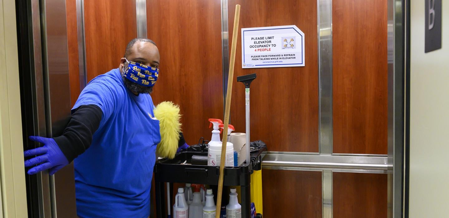 Cleaner in an elevator with cleaning supplies, blue uniform and mask