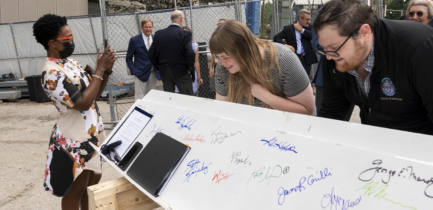 A man and woman sign a beam while another woman takes a picture on a phone