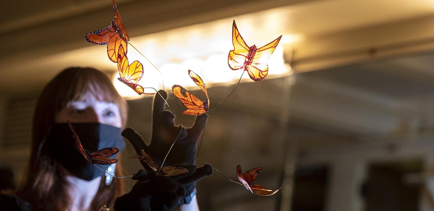 Woman with face mask holding plastic butterflies in front of light