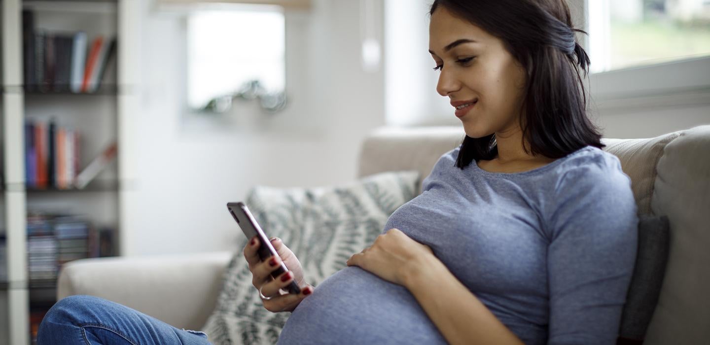 Pregnant woman using cellphone on the couch