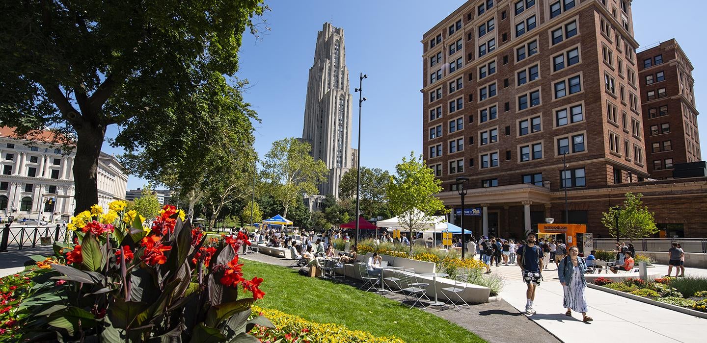 Cathedral of Learning towering behind flowerbed and busy sidewalk