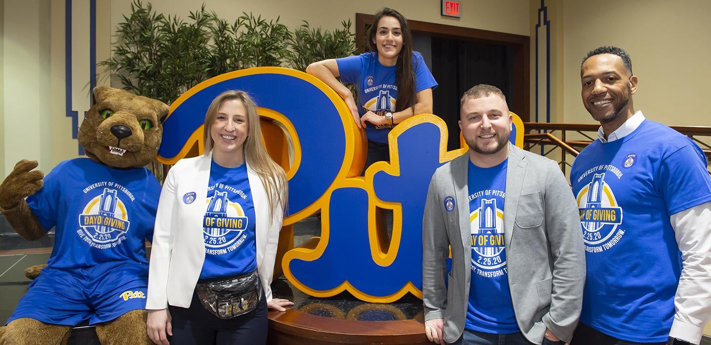 Roc posing with people wearing Pitt Day of Giving shirts next to Pitt sign