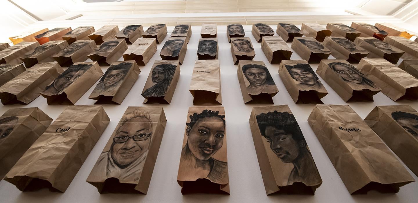 Art exhibition with drawings of people's faces on brown paper bags