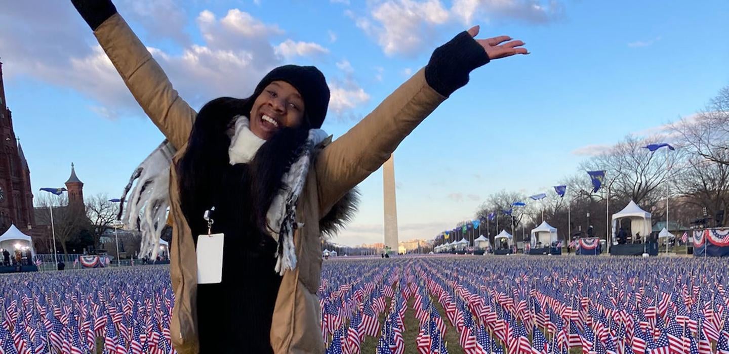 Gabriella Ogude in a black scarf and tan jacket in front of the Washington Monument