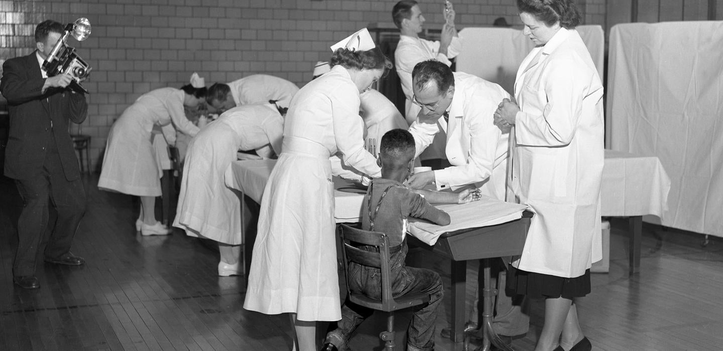 Old photo of Jonas Salk with nurses helping a child
