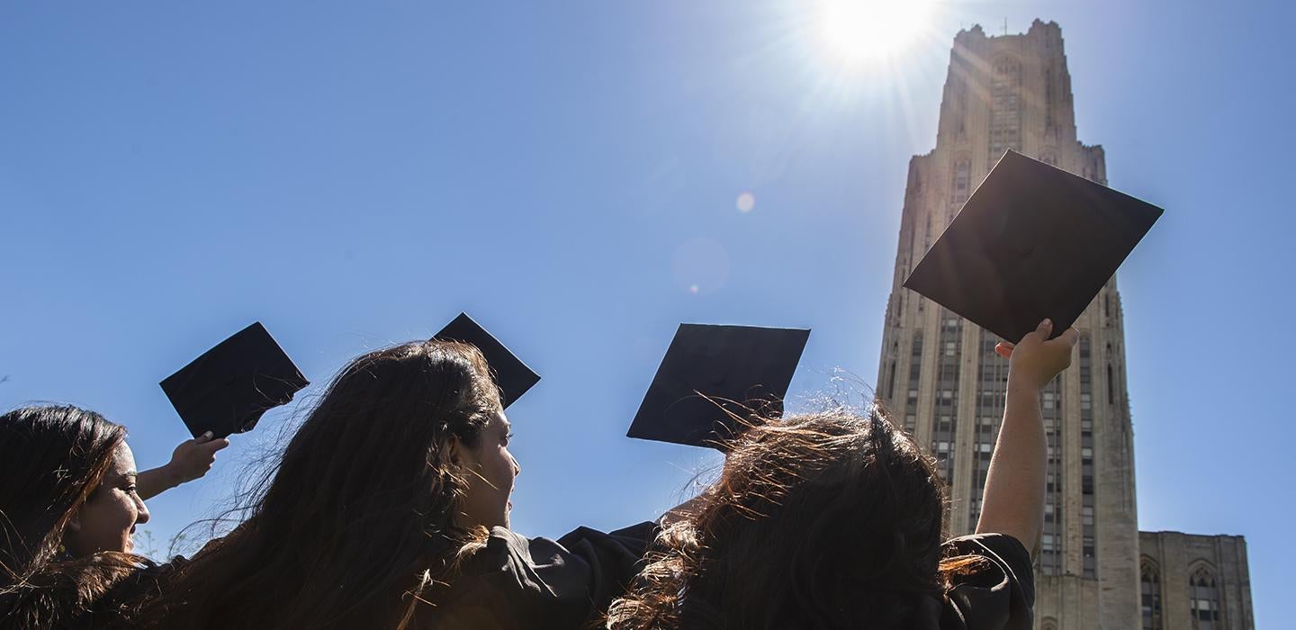 Pitt graduates pointing caps towards the Cathedral of Learning 