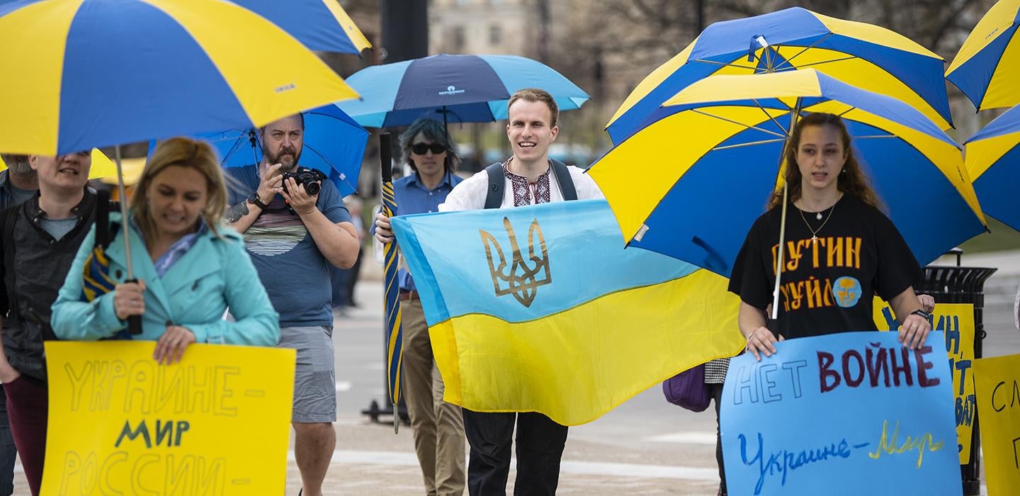 People holding blue and yellow Ukraine flags, signs and umbrellas during rally