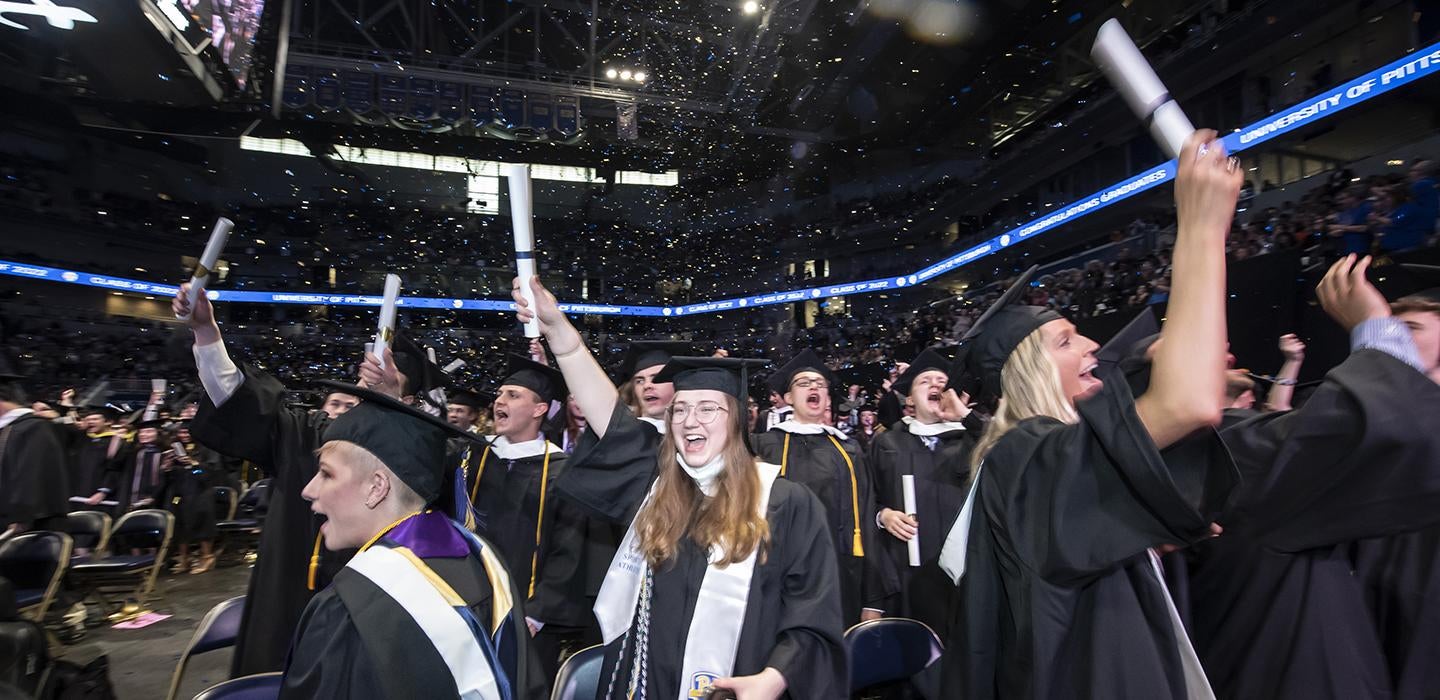 Pitt graduates cheering and holding diplomas in the air