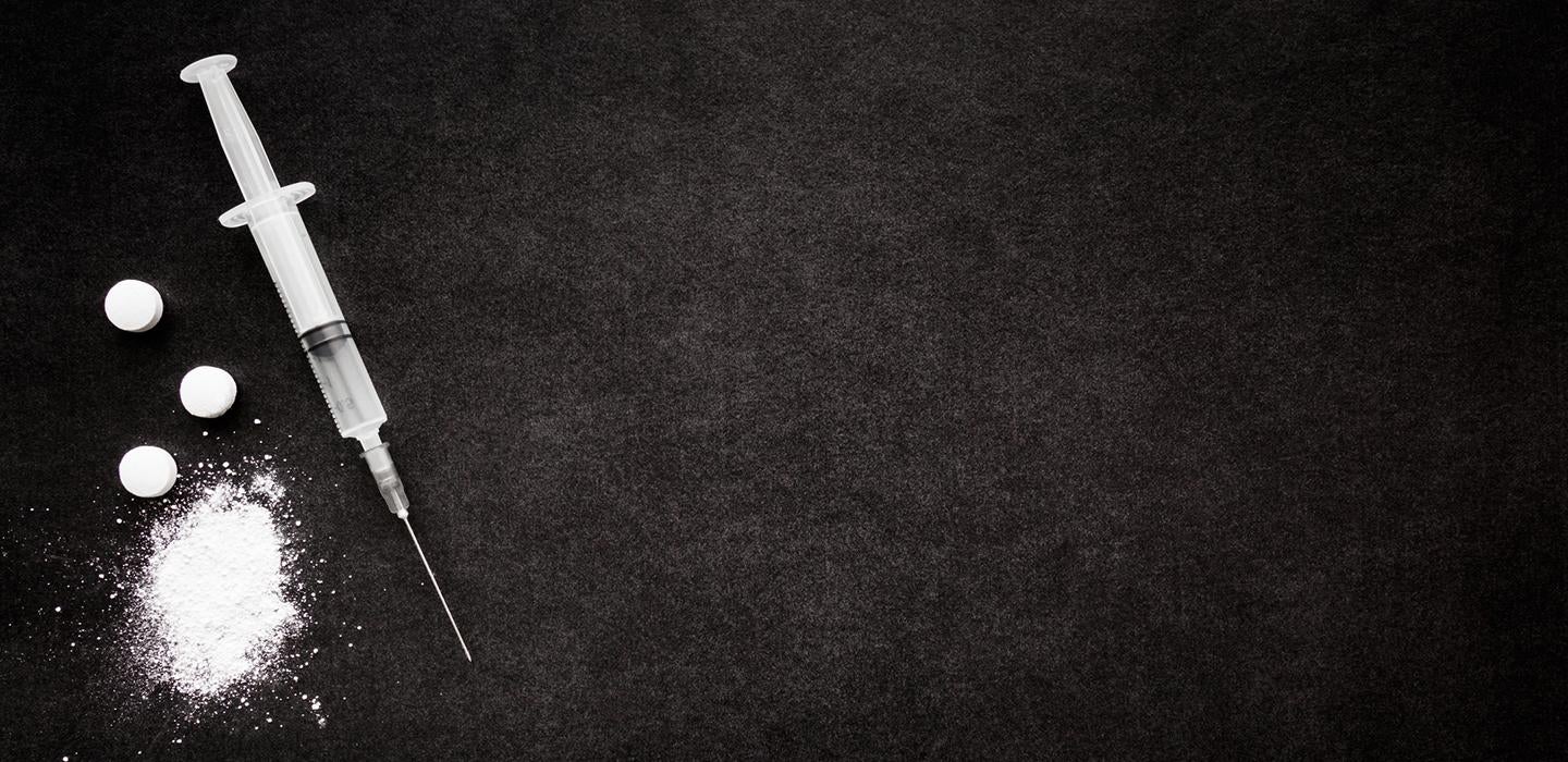 Syringe next to crushed pills in front of black background