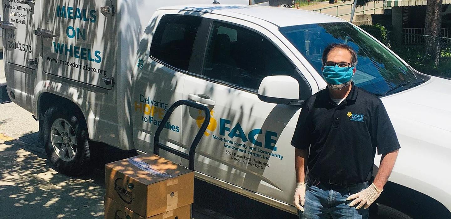 Justin LeWinter in a blue face mask standing next to a truck and a pile of cardboard boxes
