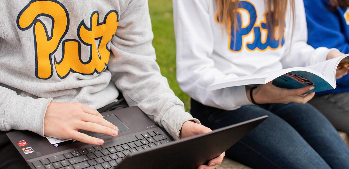 Pitt students sitting outside with laptop and book