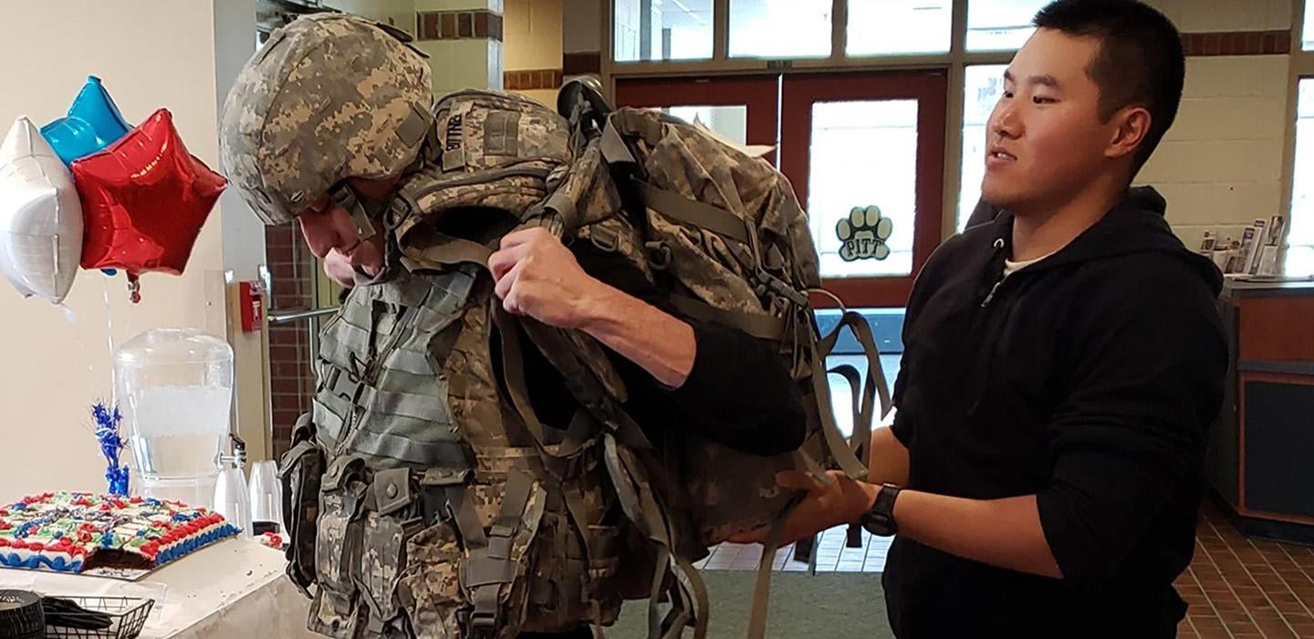 a person helping someone lift up a camo backpack