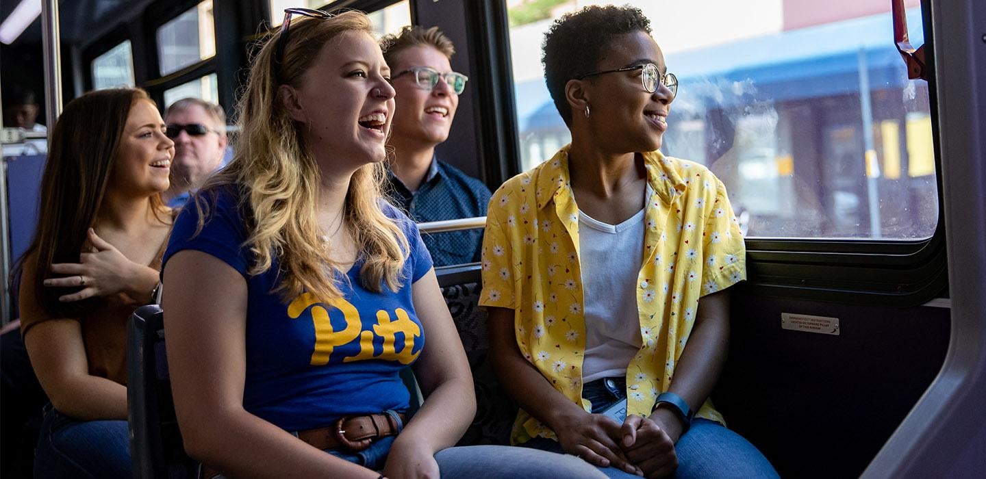 students in Pitt gear riding a bus