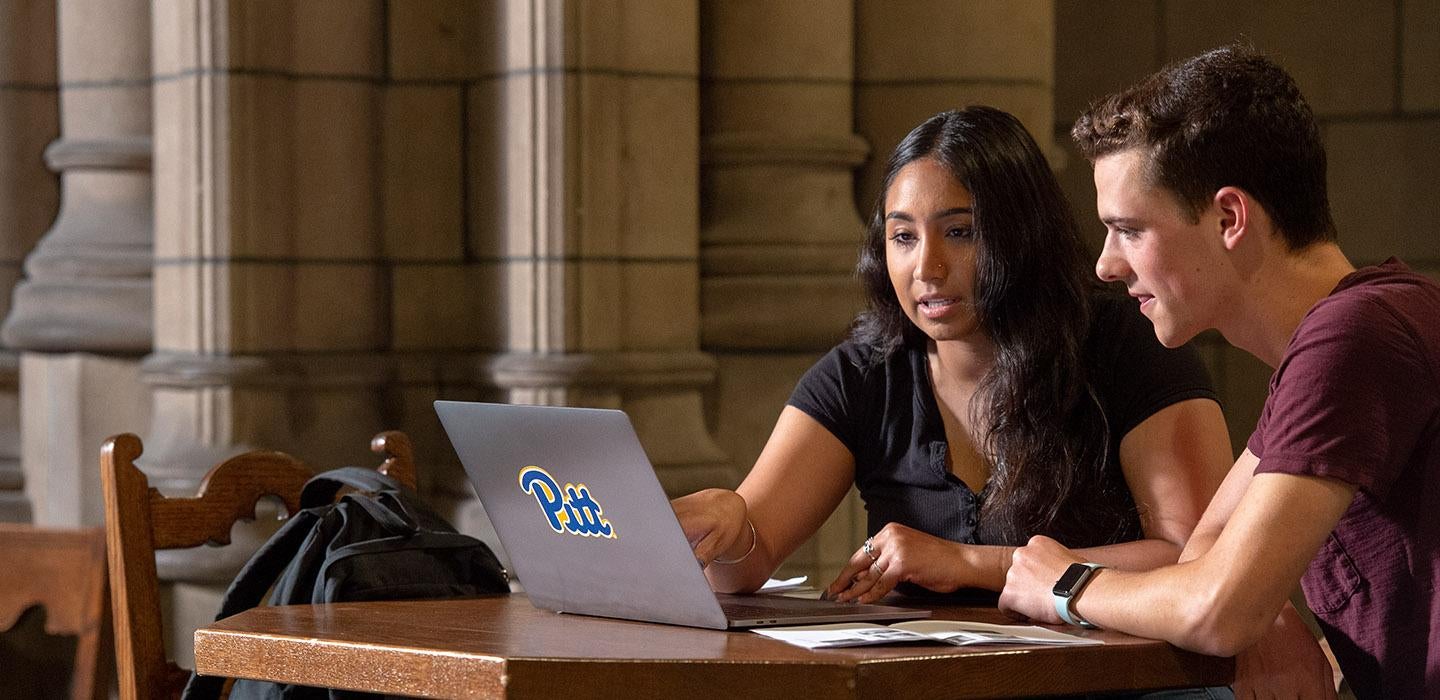 two students at a laptop with a Pitt sticker on it