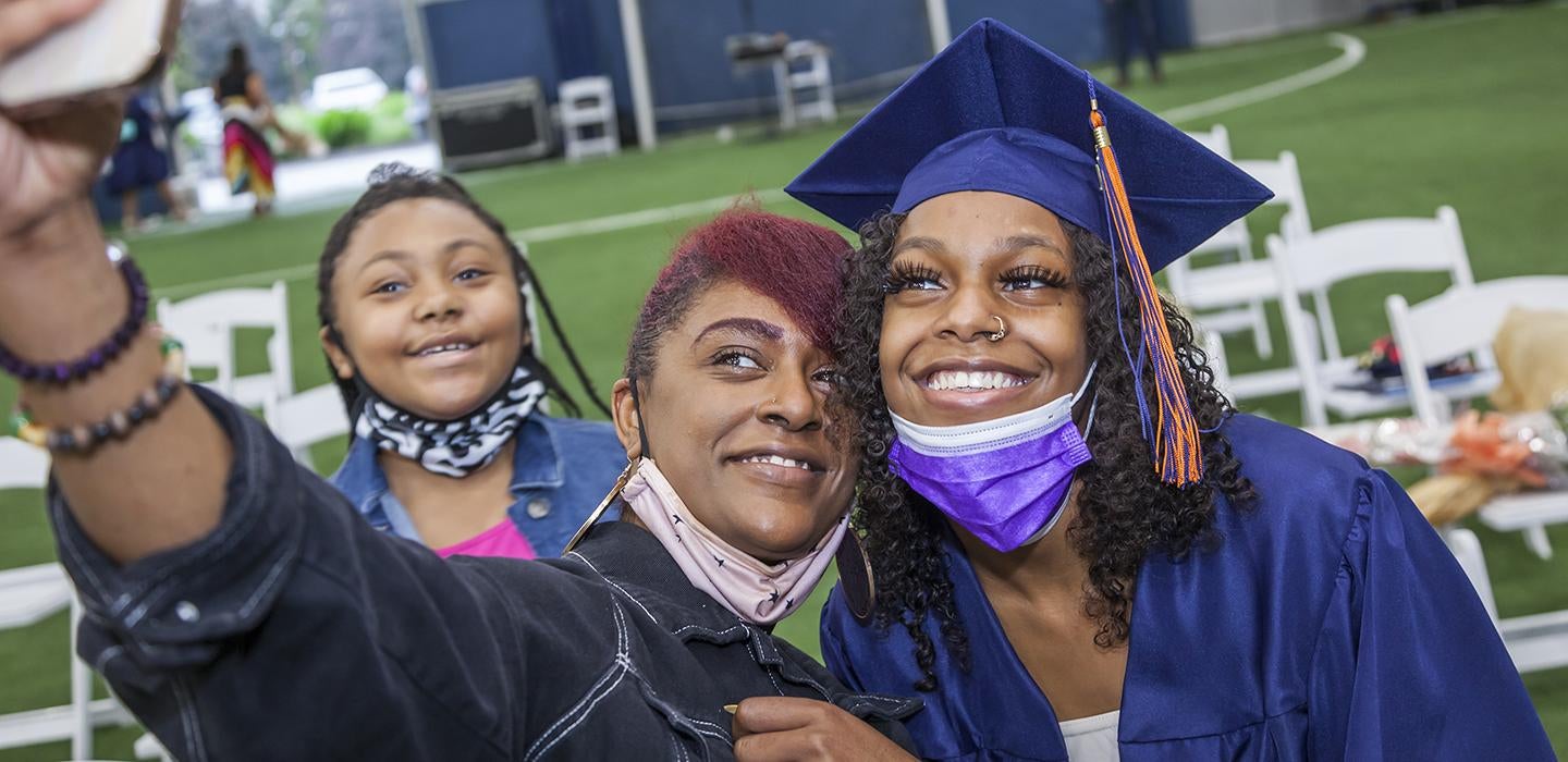 students taking a selfie, one dressed in graduation regalia