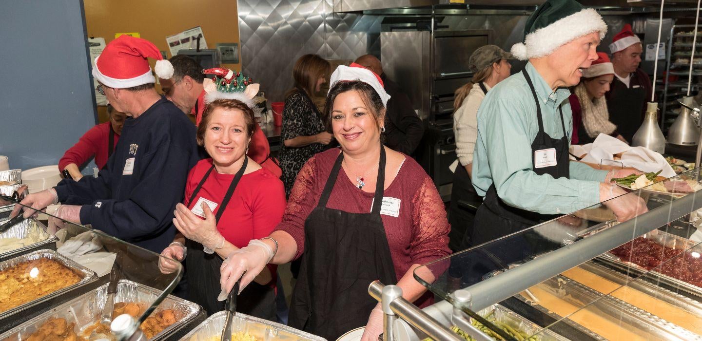 Volunteers wearing Santa hats serve food from trays.