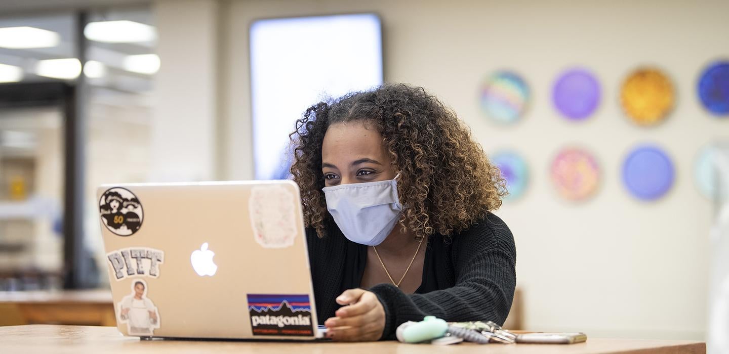 A student wearing a mask looks at a MacBook.