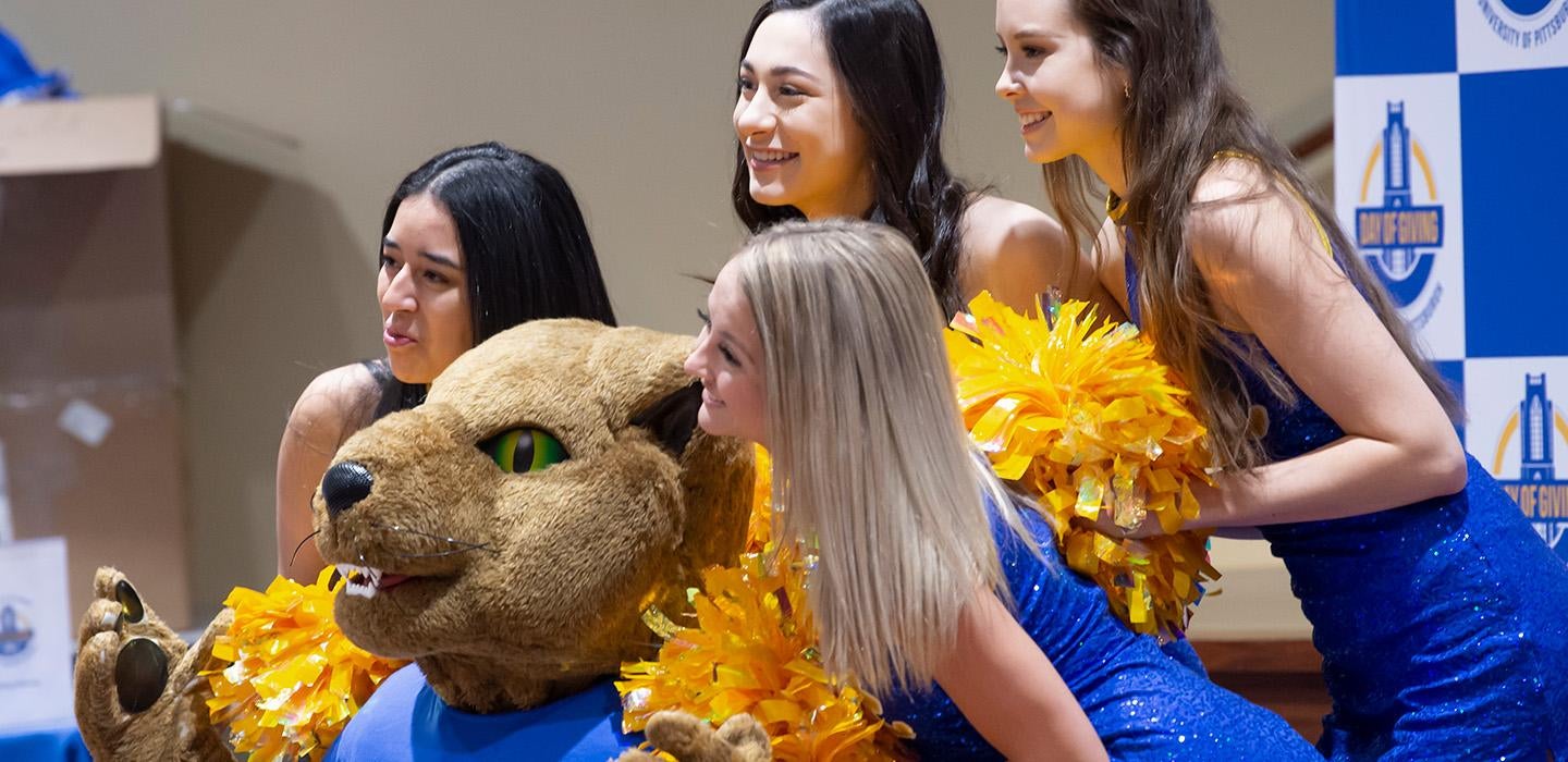 Cheerleaders with yellow pom poms pose with Roc the Panther