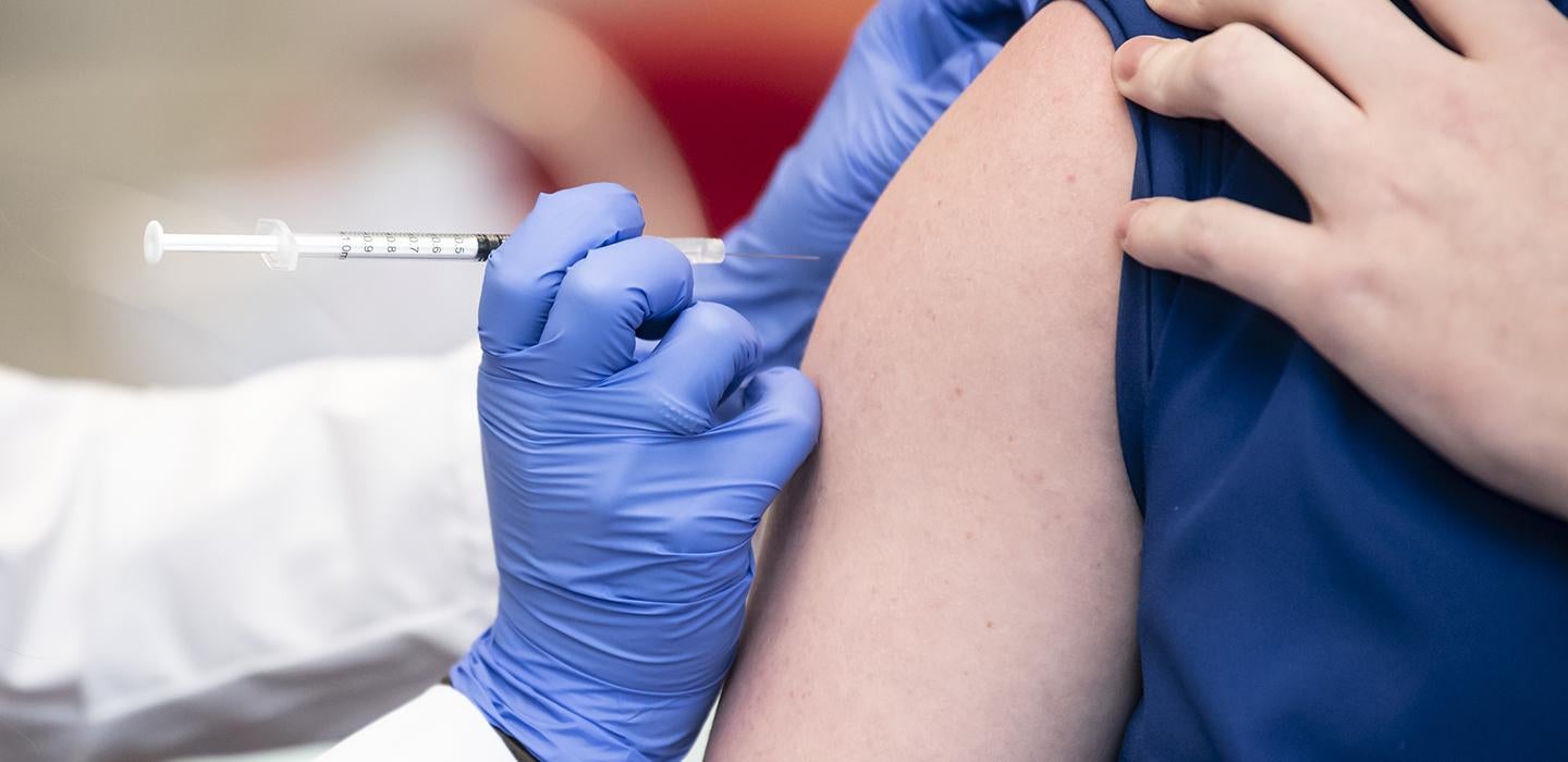 a gloved hand injecting a vaccine into an arm