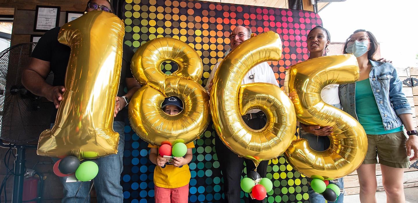 People hold up gold number balloons that spell out 1865