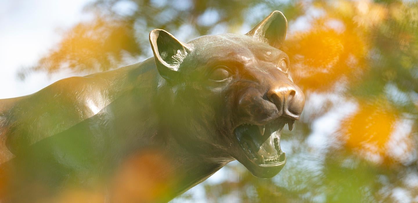 A panther statue through yellow leaves