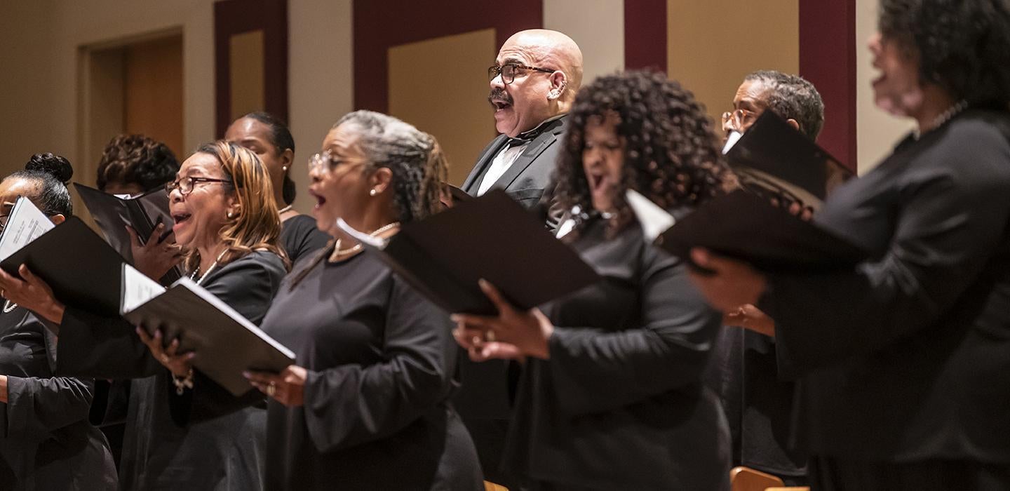 A choir wearing black sings from black folders