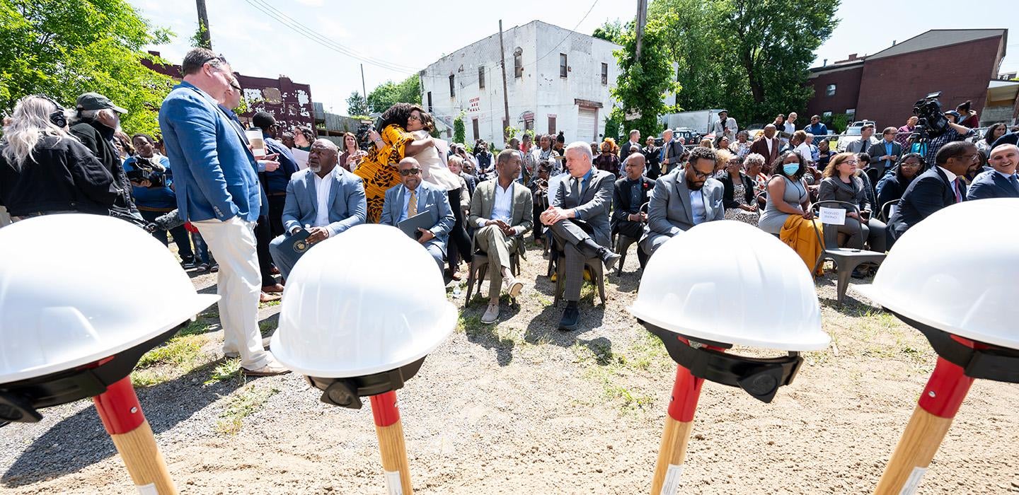 A crowd sits in chairs in front of a row of ceremonial shovels and hardhats