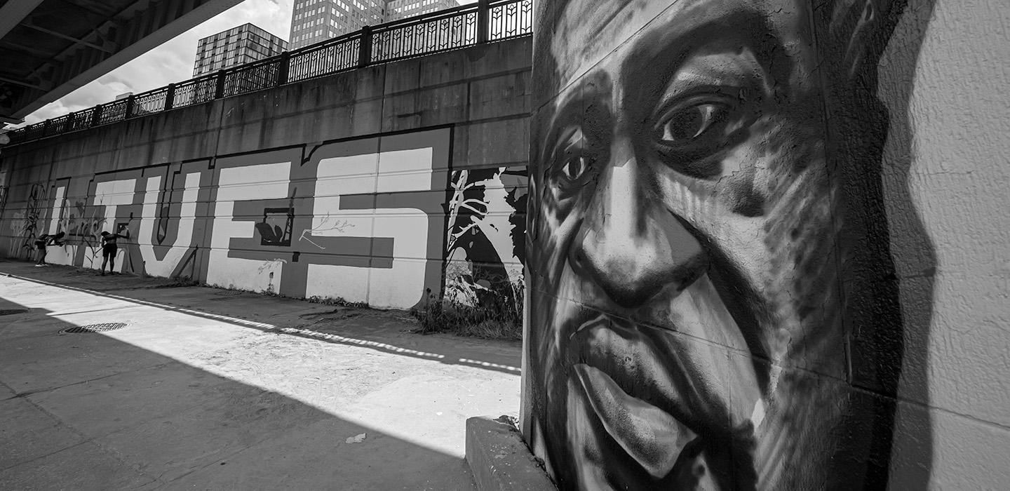 A black-and-white photo of a painting of George Floyd's face on a bridge underpass in Downtown Pittsburgh