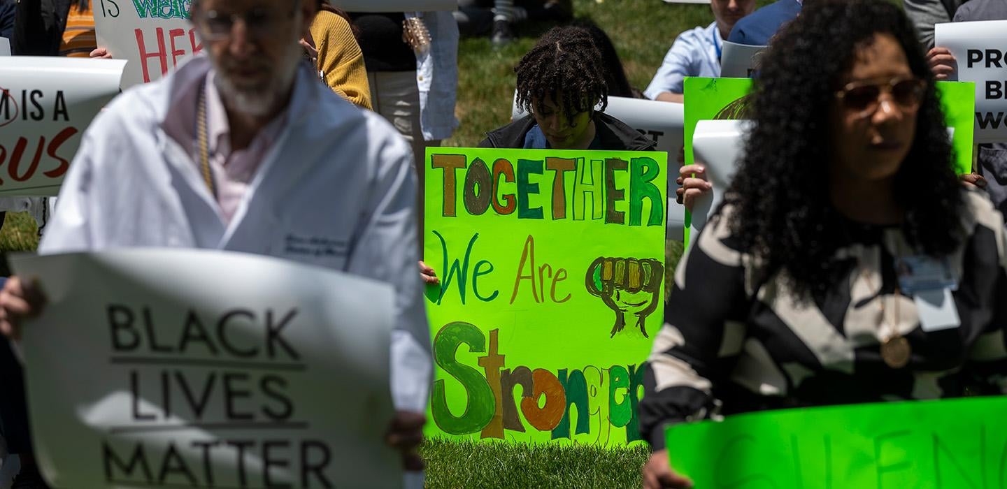 A person holds a green sign that says together we are stronger. Doctors holding signs stand around them.