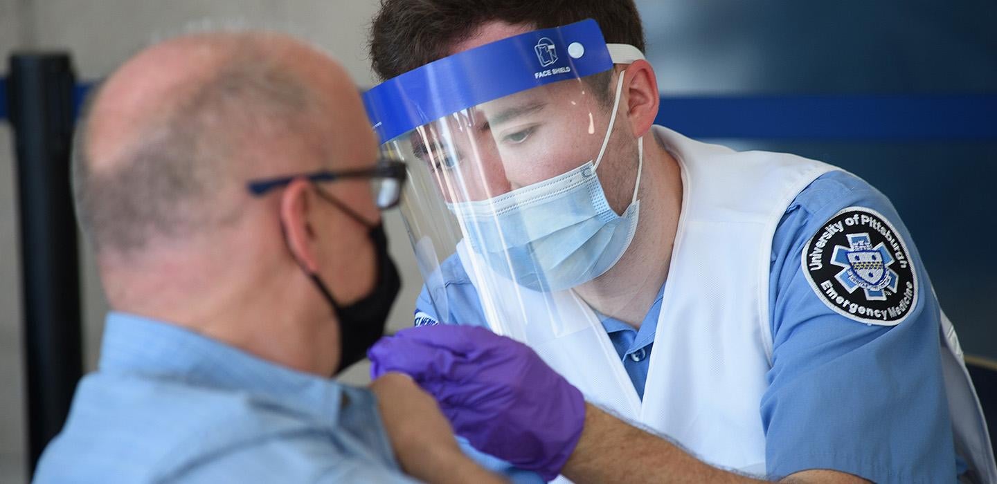 A doctor in a mask and a face shield gives a vaccine to a masked man