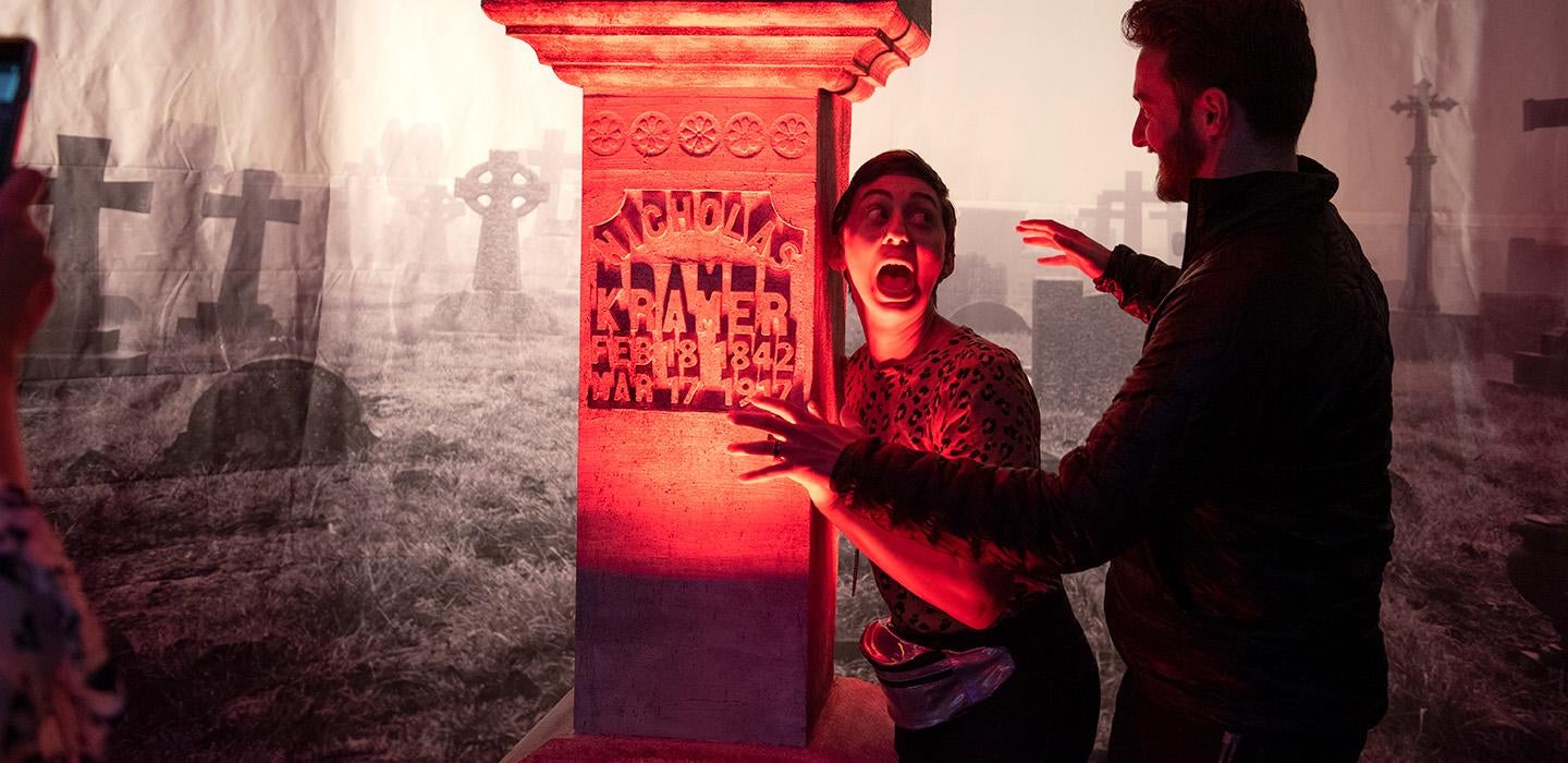 A person holds a gravestone prop and screams for a photo as a person approaches