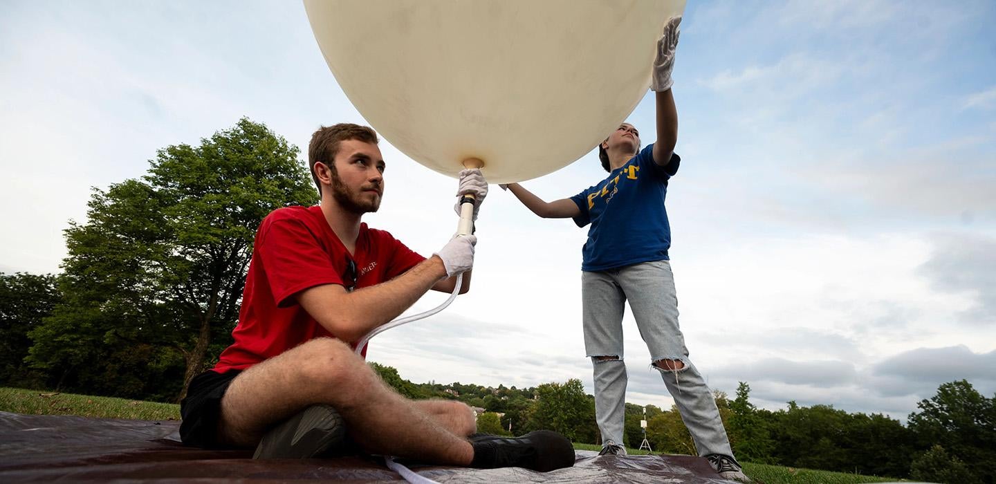 One student fills a large weather balloon with air while another holds it above her head