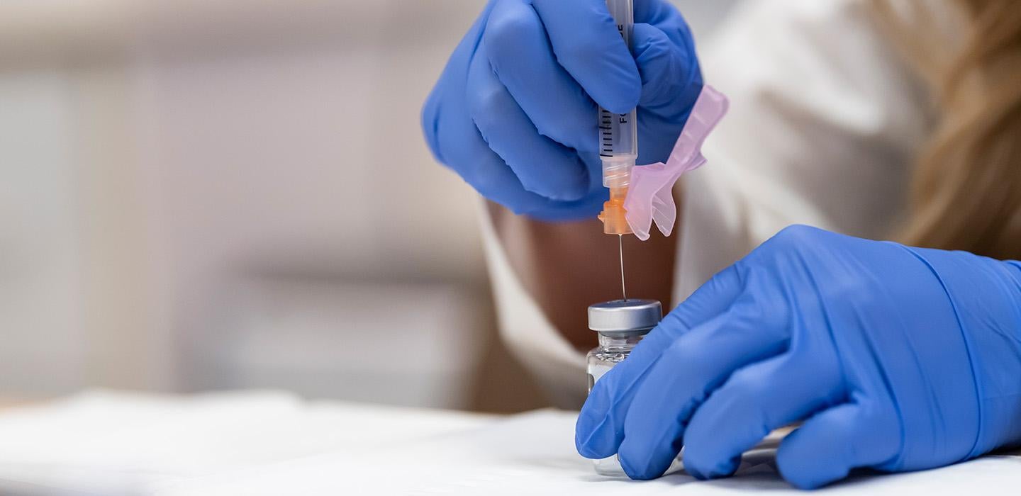 Gloved hands pull a vaccine into a syringe