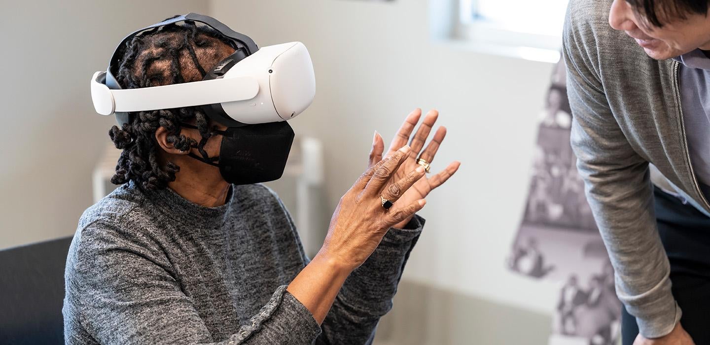 A person wearing a VR headset holds up their hands and speaks to an instructor