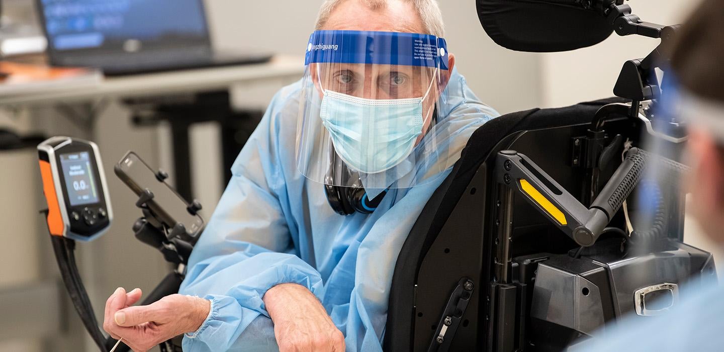 A masked person looks back from a wheelchair with mounted devices