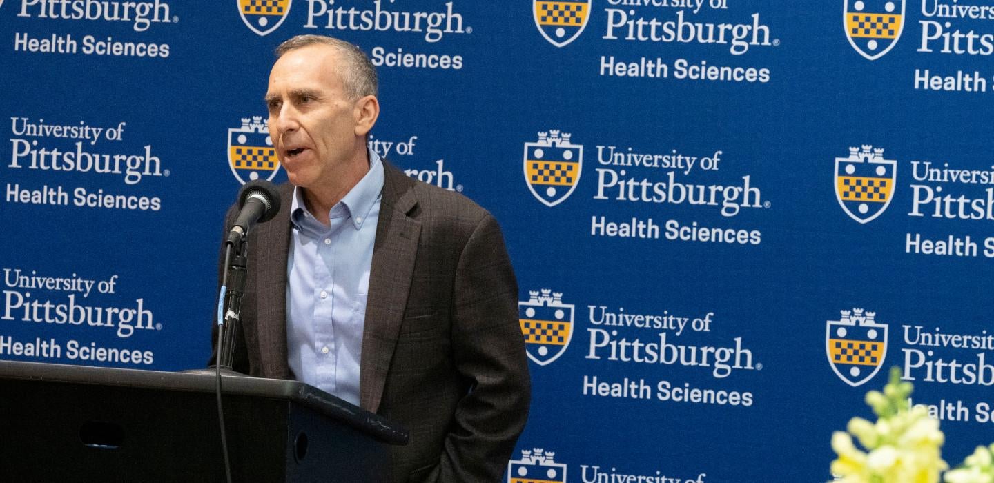 Michel Boninger speaks in front of a Pitt Health Sciences logo 