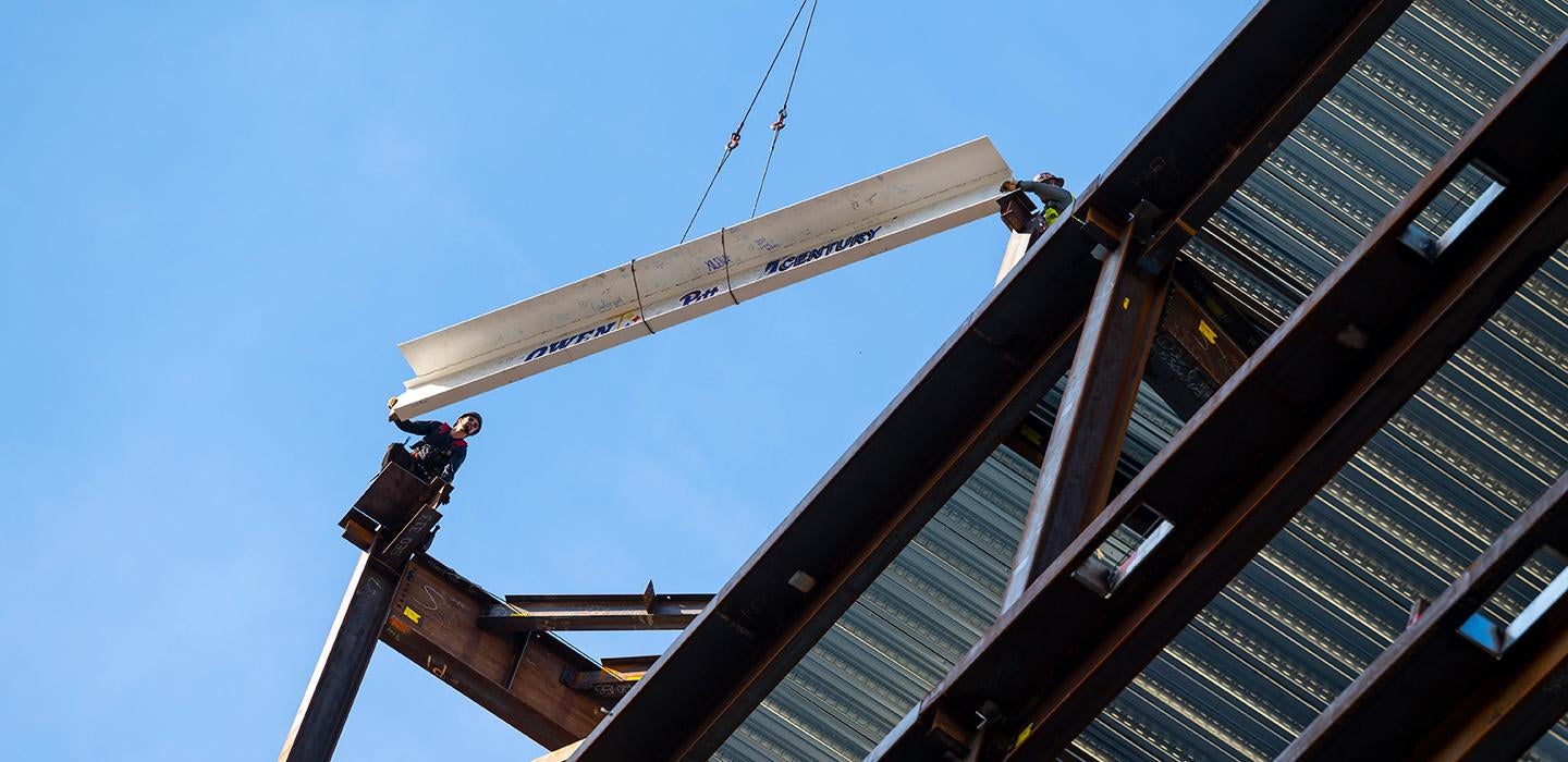 A beam is lifted to the top of a structure that is under construction