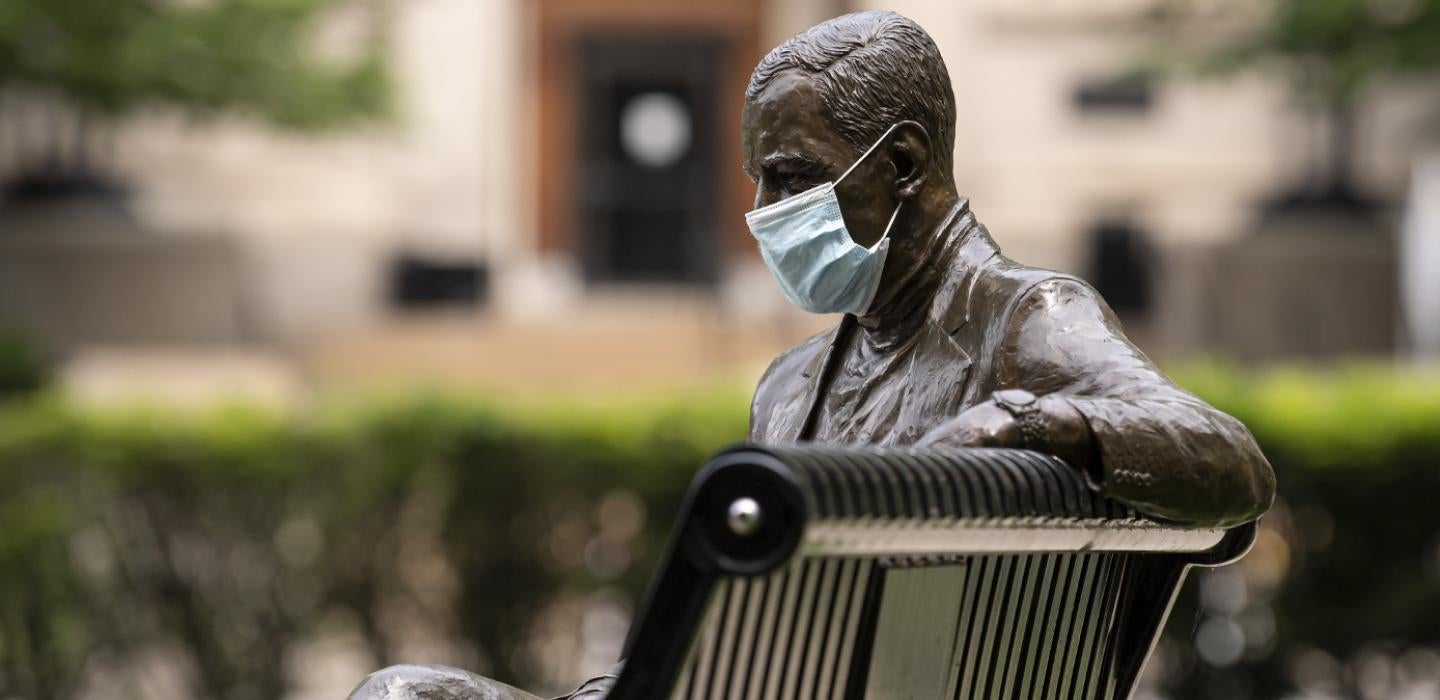 A statue sitting on a bench with a face mask