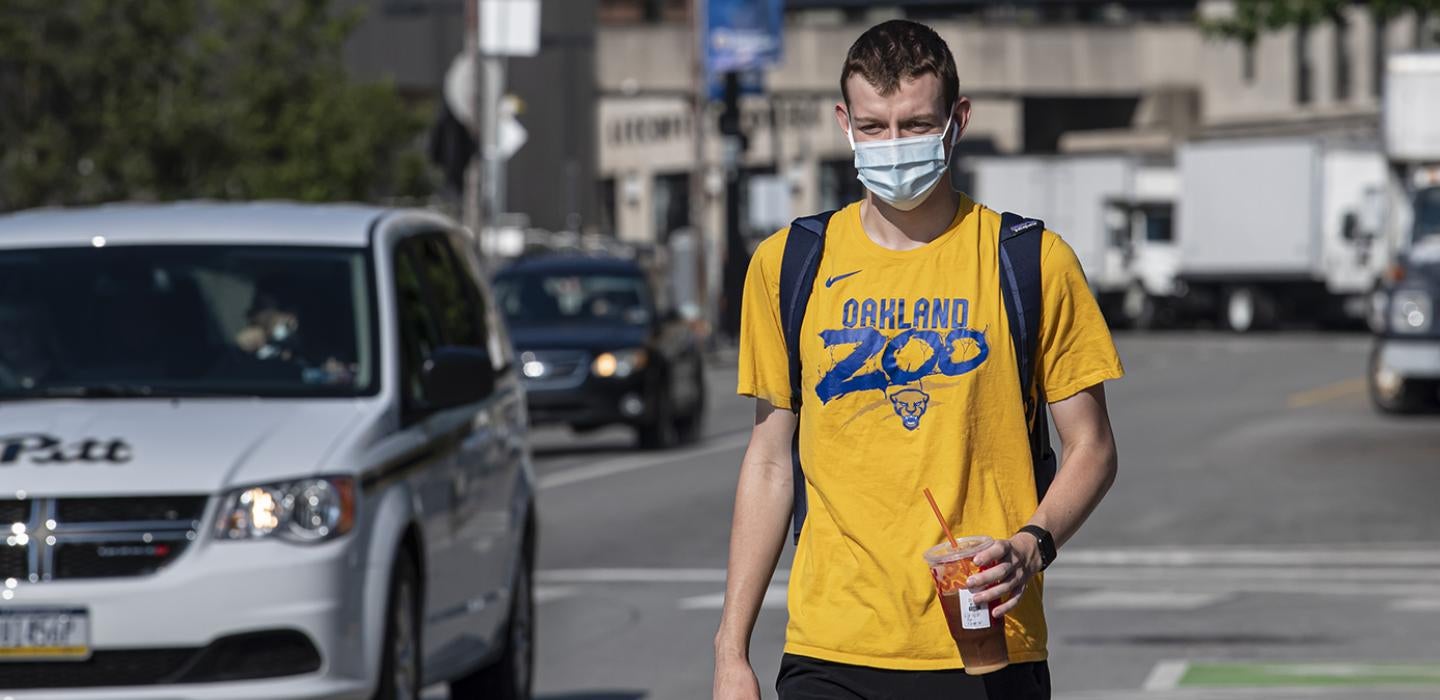 A person in an orange t-shirt and face mask walks on campus